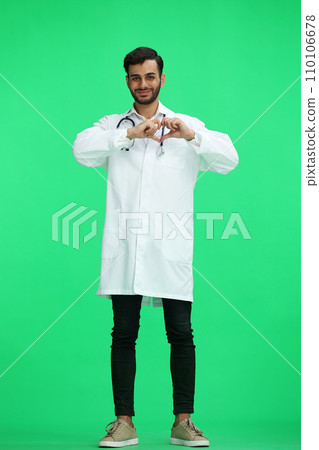 male doctor on a green background. shows a heart in full growth with his hands 110106678