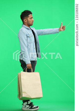 Man on a green background with shoppers show thumb up, in profile Man on a green background with shoppers show thumb up, in profile 110106692