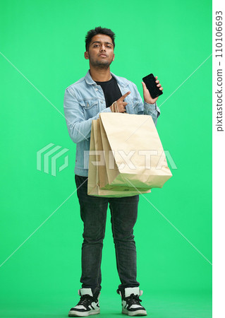 Man on a green background with shoppers show phone Man on a green background with shoppers show phone 110106693