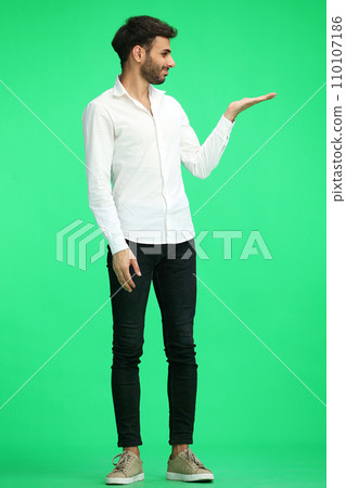 A young man on a green background in full growth shows his hand to the side 110107186