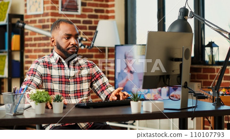 Overworked teleworker carefully typing data on computer in warm cozy living room apartment listening to tv background noise. Focused tired freelancer remotely working stressed by deadlines 110107793