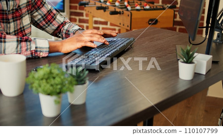 Employee remotely working from home on computer, inputing data in his brick wall apartment. African american freelancer typing on keyboard, teleworking at nice clean wooden desk, close up 110107799