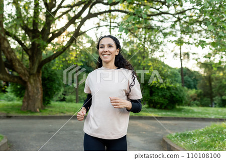 Young beautiful woman running in the evening in the park, hispanic woman with curly hair smiling contentedly, active lifestyle 110108100