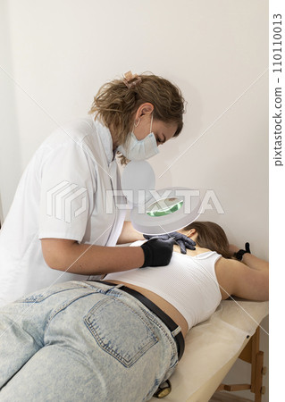 Doctor Doing Hair Removal Electrolysis Procedure On Woman's Back, Electric Epilation In Beauty Salon. Vertical Plane. Authentic Photo 110110013