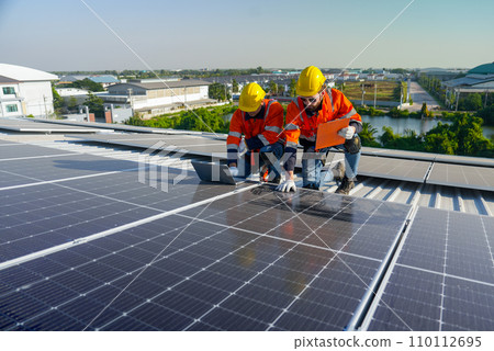 Caucasian technician workers look at laptop to check and maintenance solar cell panels on rooftop of factory or the building. Green and sustainable energy concept. Caucasian technician workers look at laptop to check and maintenance solar cell panels on rooftop of factory or the building. Green and sustainable energy concept. 110112695