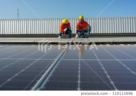 Two Caucasian technician workers sit on rooftop and discuss about the maintenance solar cell panels on rooftop of factory or the building. Green and sustainable energy concept. 110112696