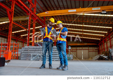 Wide shot of two Caucasian technician workers hold tablet and stand together to discuss about work in factory workplace area. Wide shot of two Caucasian technician workers hold tablet and stand together to discuss about work in factory workplace area. 110112712