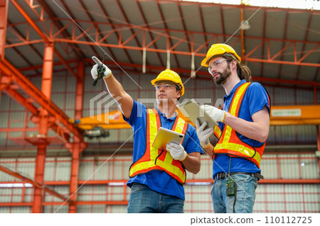 Front view of factory technician worker hold tablet and point to left direction and he stand to discuss with co-worker in workplace area. Front view of factory technician worker hold tablet and point to left direction and he stand to discuss with co-worker in workplace area. 110112725