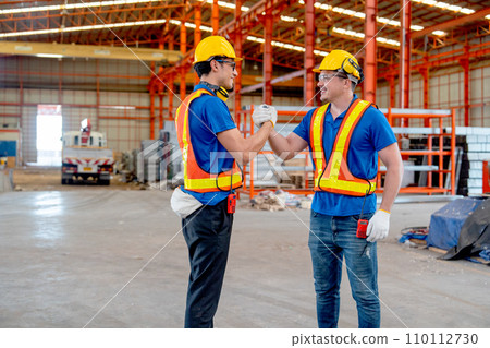 Two Caucasian technician workers hold hands and look happy in factory workplace area with backgroud of truck and the products. Two Caucasian technician workers hold hands and look happy in factory workplace area with backgroud of truck and the products. 110112730