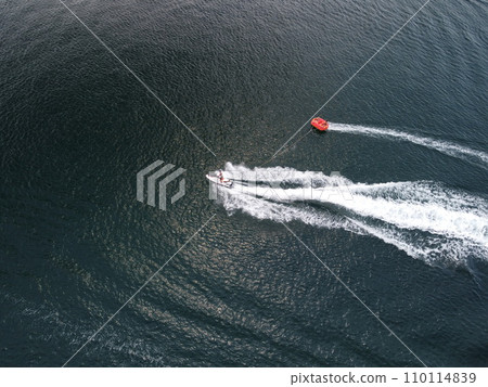 Happy people swim on air mattress behind a high speed water bike. Tourists ride on inflatable watercraft boat. Sea attraction. Water scooter skating people on large Inflatable raft. Slow motion 110114839