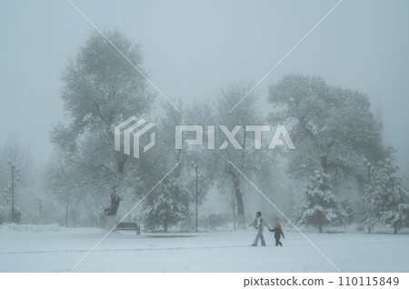 woman mother and child son walk through Park in Shymkent in Kazakhstan in winter with snow and fog 110115849