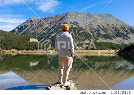 Young man standing near the lake and mountain and enjoying view of nature Young man standing near the lake and mountain and enjoying view of nature 110120358
