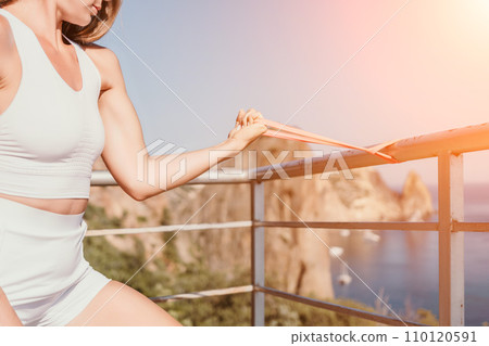 Woman sea fitness. Happy woman with long hair, fitness instructor in white doing stretching and pilates with ribbons in park near the sea. Female fitness yoga routine concept. Healthy lifestyle. 110120591