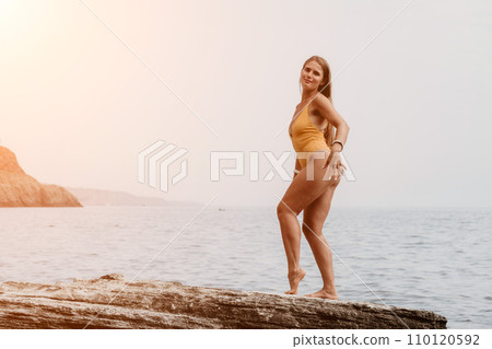 Woman sea yoga. Back view of free calm bliss satisfied woman with long hair standing on top rock with yoga position against of sky by the sea. Healthy lifestyle outdoors in nature, fitness concept. 110120592