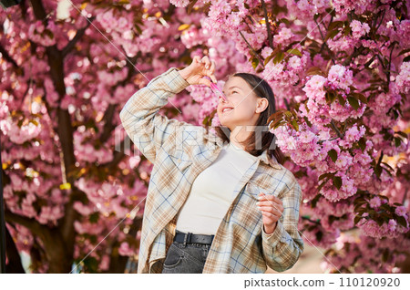 Woman allergic suffering from seasonal allergy at spring. Smiling woman with clothespin clipped to his nose - symbolic gesture of his inability to breathe due to nasal congestion near blooming tree. 110120920