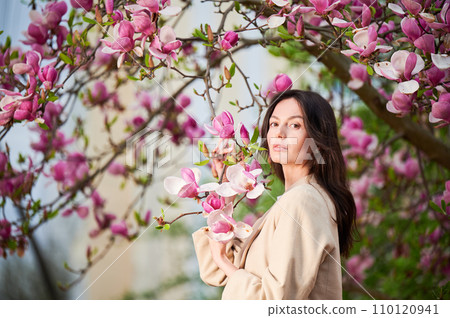 Woman allergic enjoying after treatment from seasonal allergy at spring. Portrait of happy young woman in front of blooming magnolia tree at springtime. Spring allergy concept. Woman allergic enjoying after treatment from seasonal allergy at spring. Portrait of happy young woman in front of blooming magnolia tree at springtime. Spring allergy concept. 110120941