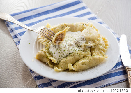 cooked dumplings with meat, spices and sour cream, in a plate on a light wooden table. cooked dumplings with meat, spices and sour cream, in a plate on a light wooden table. 110121890