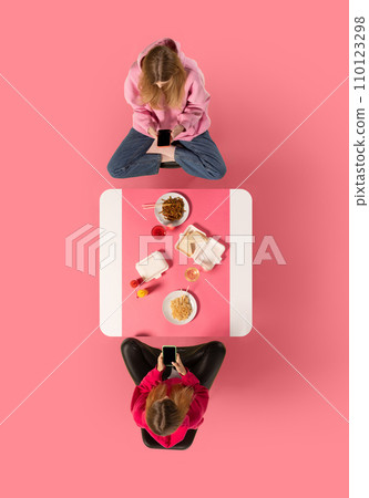Creative collage. Two young woman, friends sitting at Asian cafe and eating delicious food while speaking against pink background. Creative collage. Two young woman, friends sitting at Asian cafe and eating delicious food while speaking against pink background. 110123298