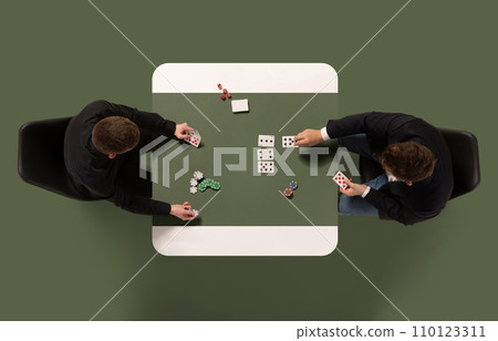Creative collage. Top view of two persons playing cards, gambling on table against green, khaki color background. Copy space. Creative collage. Top view of two persons playing cards, gambling on table against green, khaki color background. Copy space. 110123311