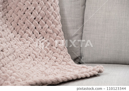 Knitted large plaid blanket in dusty rose light grayish-red color on the sofa. Knitted large plaid blanket in dusty rose light grayish-red color on the sofa. 110123344