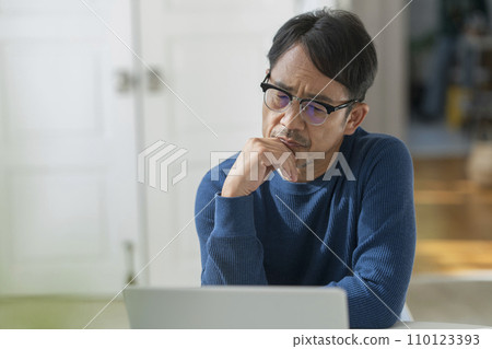 A man in his mid-50s thinking while looking at a laptop screen 110123393