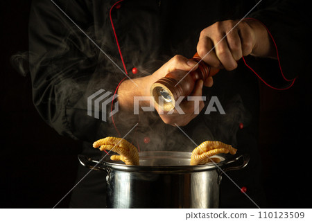 The chef adds pepper to a pot of boiling chicken legs. Concept of preparing a delicious side dish in a restaurant or hotel kitchen The chef adds pepper to a pot of boiling chicken legs. Concept of preparing a delicious side dish in a restaurant or hotel kitchen 110123509