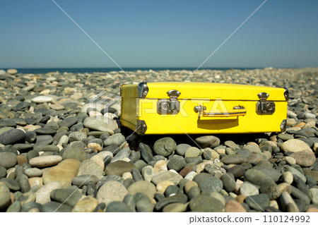 Yellow vintage suitcase resting by the seaside. Retro style suitcase in yellow color. A symbol of whimsical adventures and the promise of sunlit discoveries and summer journeys. 110124992
