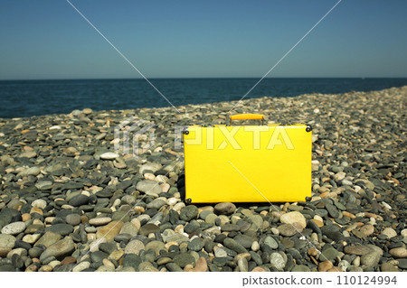 Yellow vintage suitcase resting by the seaside. Retro style suitcase in yellow color. A symbol of whimsical adventures and the promise of sunlit discoveries and summer journeys. 110124994