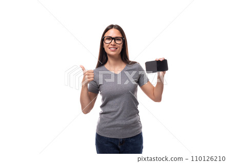 young brunette european woman dressed in a gray basic t-shirt shows the smartphone screen 110126210