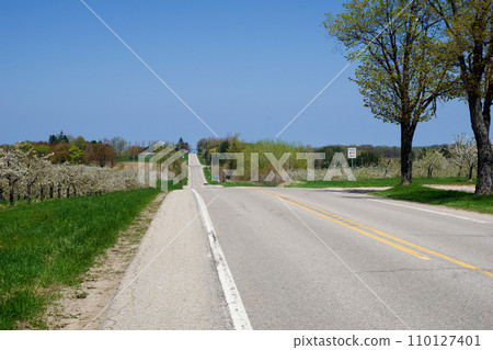 KEWADIN, MICHIGAN, UNITED STATES - MAY 16, 2018: Hilly country road in northern Michigan with cherry trees in bloom along the roadside KEWADIN, MICHIGAN, UNITED STATES - MAY 16, 2018: Hilly country road in northern Michigan with cherry trees in bloom along the roadside 110127401