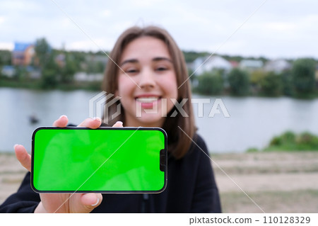 Female hands hold a smartphone with a blank screen to replace it with a text message or informational content. Empty phone space to copy promotional content. Phone in hand in an urban environment Female hands hold a smartphone with a blank screen to replace it with a text message or informational content. Empty phone space to copy promotional content. Phone in hand in an urban environment 110128329
