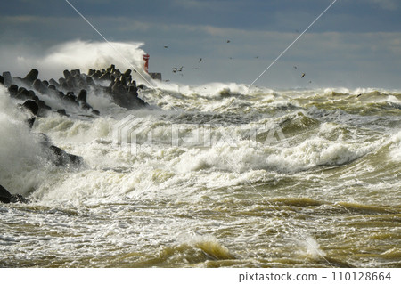 Storm at sea, high waves crashing against the concrete breakwaters of the port, white splashes 110128664