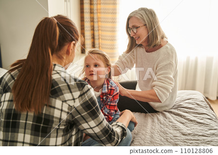 Senior woman brushing hair of little girl while talking with her daughter Senior woman brushing hair of little girl while talking with her daughter 110128806