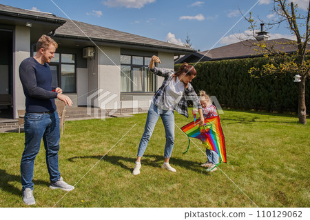 Happy family of mother, father and daughter playing with rainbow kite at summer 110129062