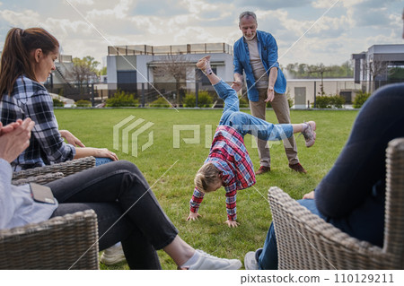 Happy family of three generations looking at little girl standing at her hands Happy family of three generations looking at little girl standing at her hands 110129211