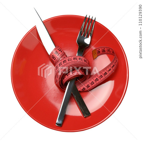 Red round plate and fork and knife wrapped in green measuring tape 110129390
