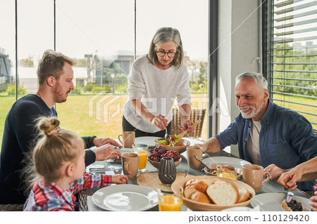 Happy extended family talking while having lunch together in dining room 110129420