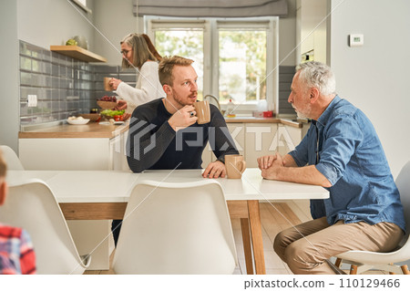 Mature father and young son drinking coffee and talking at the light kitchen 110129466