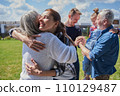 Smiling daughter embracing her senior mother while standing at the green grass lawn 110129487