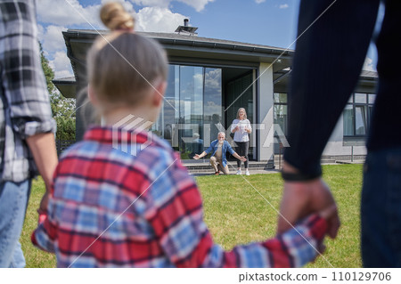 Little girl holding hands of father and mother while meeting her senior grandparents 110129706