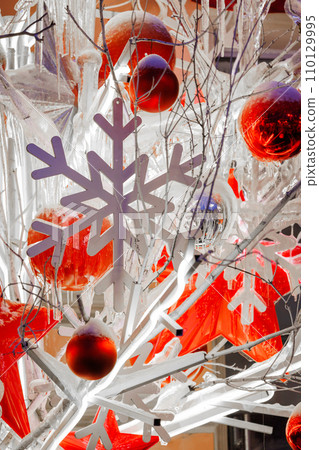 Close-up footage of Christmas Decorations on a Snow-Covered Spruce Tree in dusk, It's snowing, snowflakes are falling, red glass balls and stars, artificial snowflakes, illumination Close-up footage of Christmas Decorations on a Snow-Covered Spruce Tree in dusk, It's snowing, snowflakes are falling, red glass balls and stars, artificial snowflakes, illumination 110129995