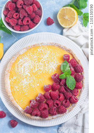 Lemon tart, garnished with fresh raspberry, icing sugar, mint, on white plate, vertical top view 110130590