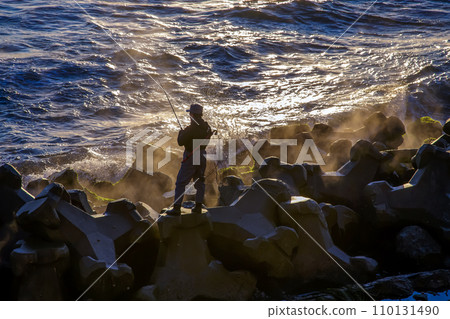 A fisherman dangles his rod into the sea while basking in the morning sun. 110131490