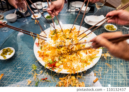 People mixing and tossing yusheng or yee sang during Chinese New Year dinner celebration. Slow shutter speed with motion blur intended. 110132437