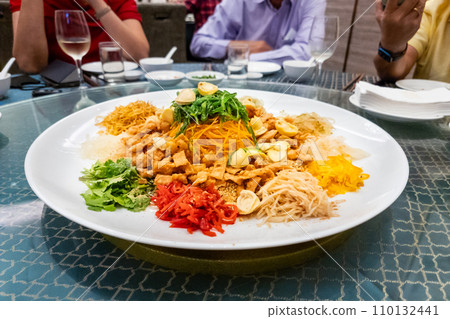 Serving of auspicious yusheng or yee sang with abalone in restaurant during Chinese New Year celebration with diners seated. 110132441