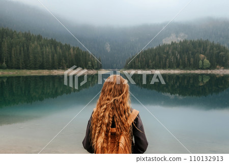 Woman Standing Alone on Shore of Mountain Lake 110132913