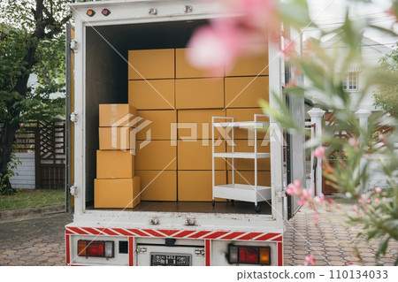 Moving cardboard boxes in an open car trunk outdoors. White delivery van for logistic transport service. House relocation scene with boxes. Moving Day Concept. Moving cardboard boxes in an open car trunk outdoors. White delivery van for logistic transport service. House relocation scene with boxes. Moving Day Concept. 110134033