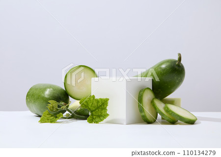 A white cube placed on white surface with green leaves and winter melon slices. Glamour minimal pedestal for beauty, cosmetic product presentation A white cube placed on white surface with green leaves and winter melon slices. Glamour minimal pedestal for beauty, cosmetic product presentation 110134279