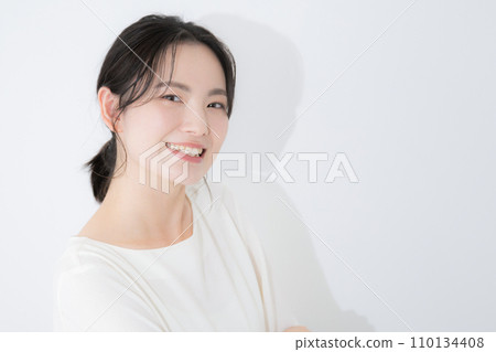一位年輕女子看著鏡頭，在白牆前微笑的特寫半身像 110134408