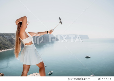 Digital nomad, Business woman working on laptop by the sea. Pretty lady typing on computer by the sea at sunset, makes a business transaction online from a distance. Freelance, remote work on vacation 110134683